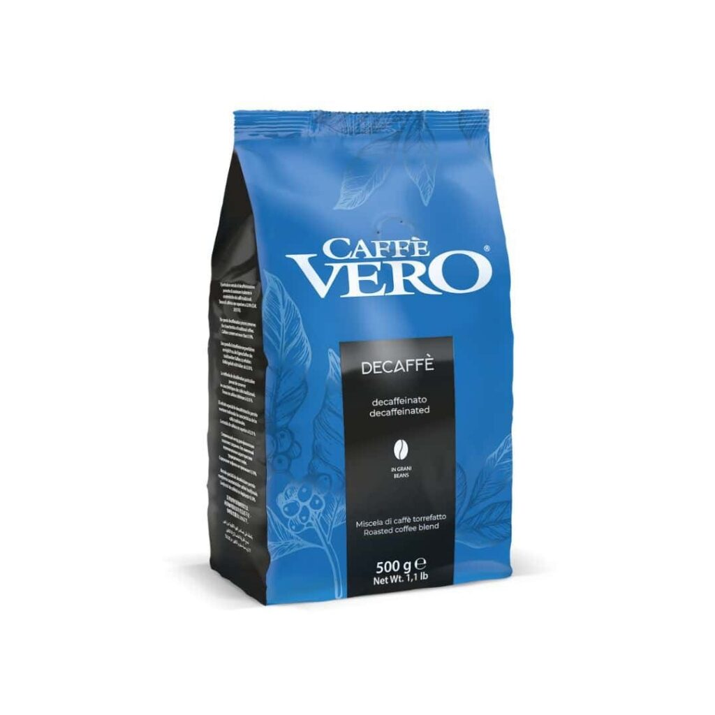 שקית של 500 גרם של פולי קפה נטולי קפאין Caffe Vero Decaff עומדת זקופה, ועליה טקסט לבן ואיורים עדינים של שיחי קפה על גבי האריזה הכחולה — מושלמת להכנת כוס קפה מושלמת במכונת הקפה שלכם או במטחנה האהובה עליכם. | אספרסימו
