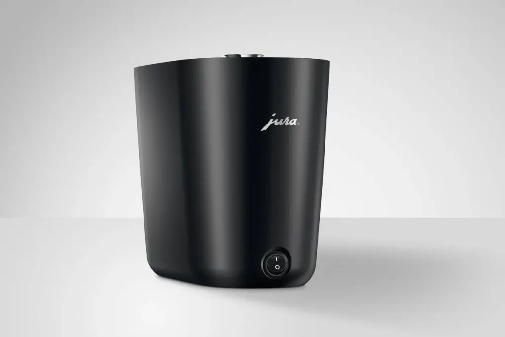 מכשיר מחמם כוסות Jura Cup Warmer S לבן ומלוטש, עם כפתור הפעלה בחלקו הקדמי התחתון ולוגו Jura מעליו, על רקע בהיר ופשוט. | אספרסימו