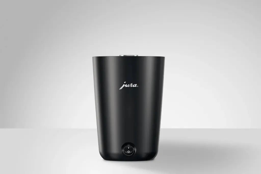 מחמם כוסות Jura Cup Warmer S לבן ומלוטש מונח על משטח לבן על רקע אפור בהיר, כאשר לוגו Jura נראה בחזיתו. | אספרסימו