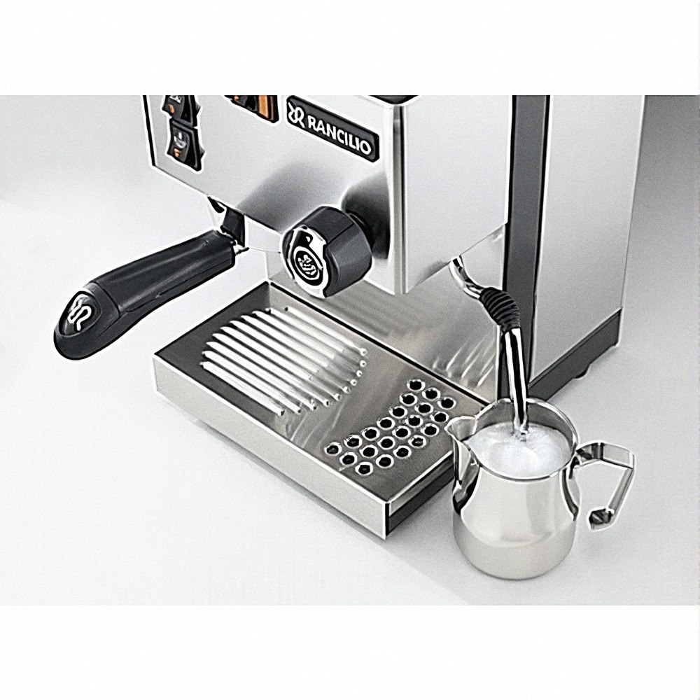 תקריב של מכונת אספרסו מתוצרת Rancilio המקציפה חלב בקנקן קטן מנירוסטה. ניתן לראות את מסנן הקפה (פורטפילטר) ואת מוט האדים של המכונה, יחד עם מגש טפטוף מתכתי, המדגישים את תהליך הכנת קפה איכותי בעל ארומה משובחת. | אספרסימו