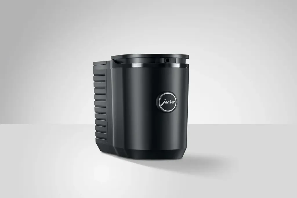 מקרר חלב Cool Control בנפח 0.6 ליטר בצבע שחור למכונות קפה JURA, עם לוגו כסוף בחזיתו, ניצב על משטח בהיר על רקע אפור חלק. | אספרסימו