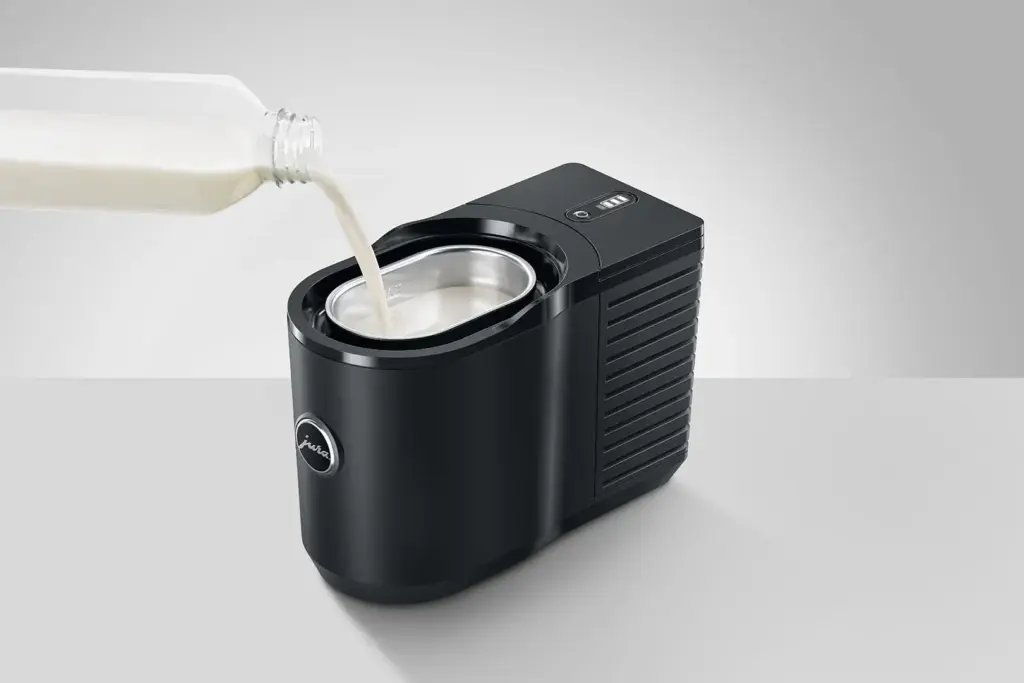 בקבוק חלב נשפך לתוך מקרר החלב Jura Cool Control (0.6 ליטר, שחור) – מכשיר שולחני עם מיכל נירוסטה – המוצב על רקע אפור אחיד. | אספרסימו